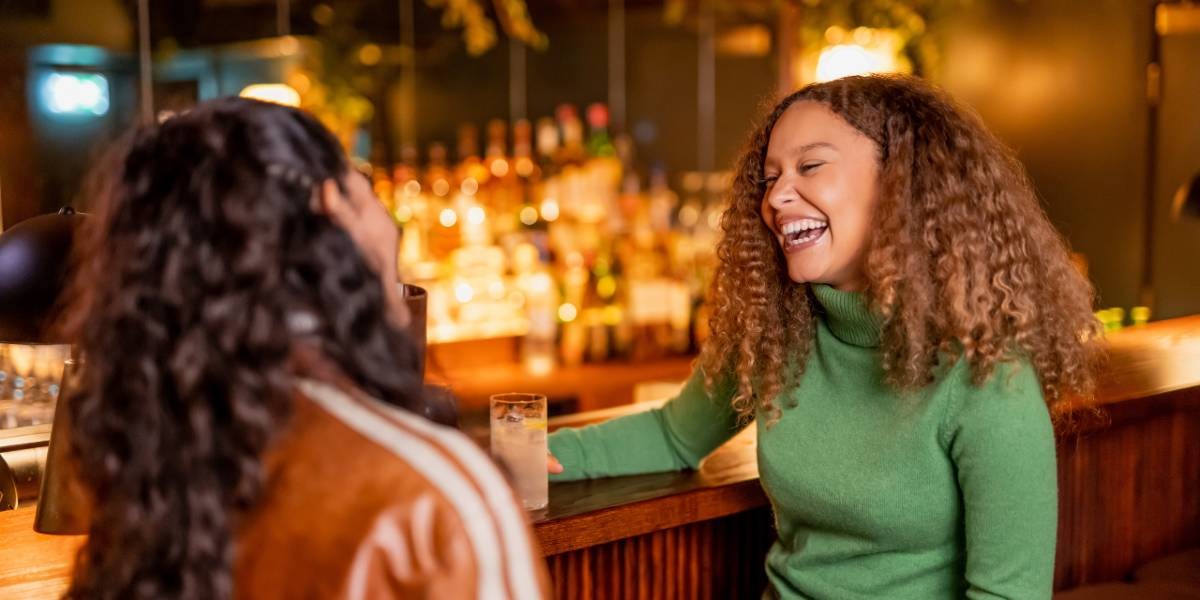 Two girls laughing sat at a bar