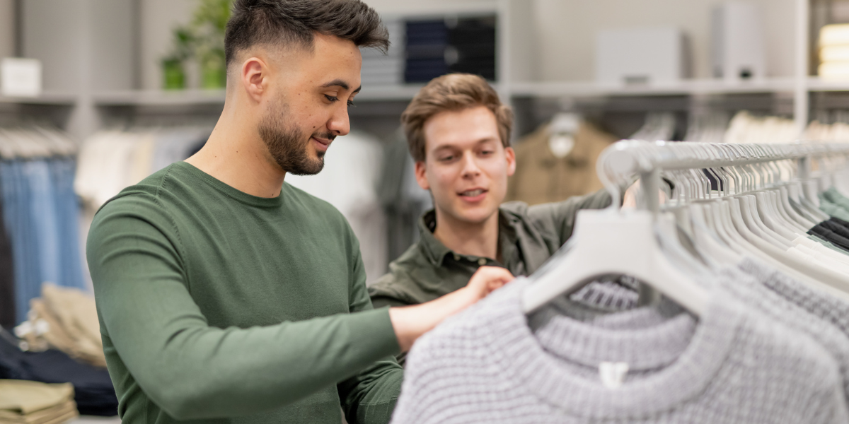 two men browsing through a rack of jumpers