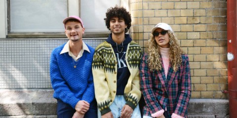 Three people dressed in vintage clothing against a brick wall