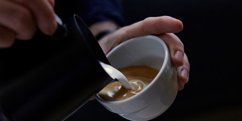 Hand pouring milk into a cup of coffee