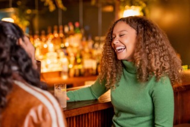 Two girls laughing sat at a bar