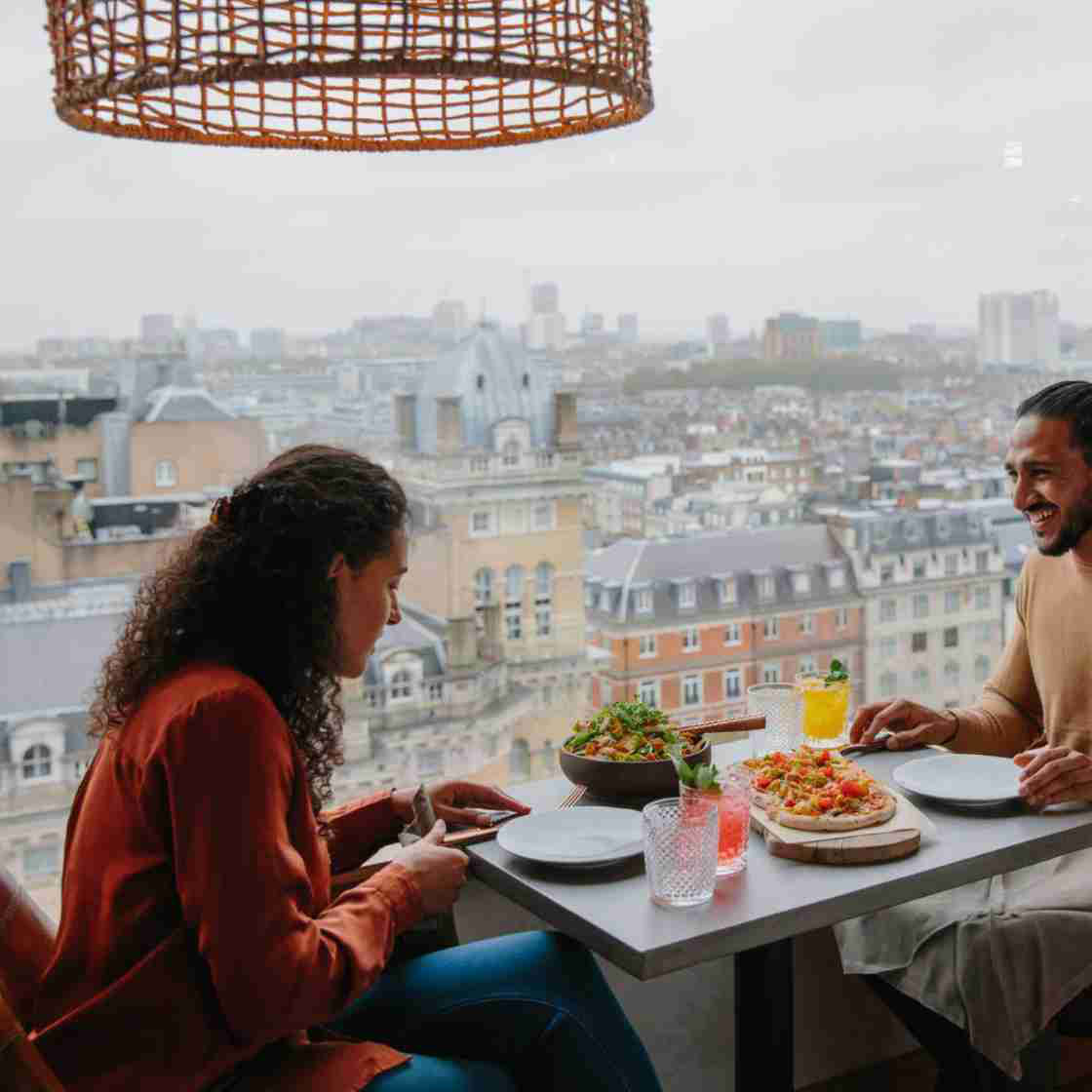 Couple sat at a table eating a meal next to a window with a rooftop view